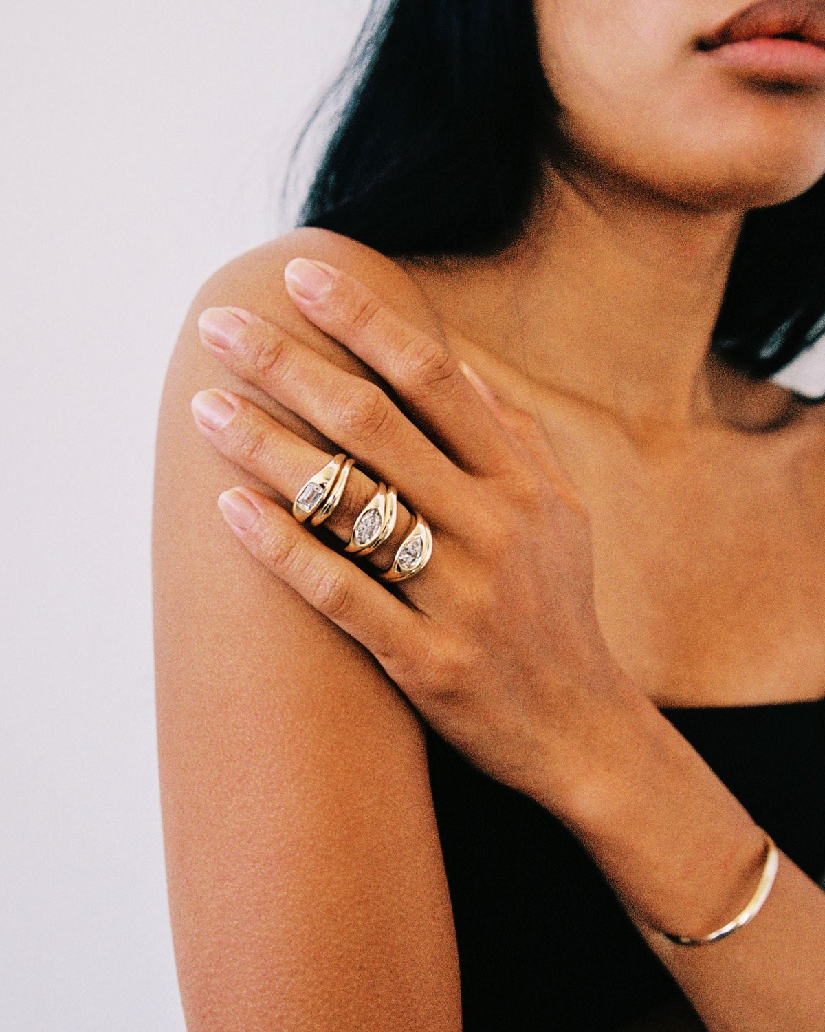 Hand wearing three chunky gold rings with flush-set diamonds in emerald, elongated, and pear shapes